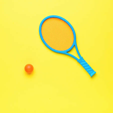 A children's badminton racket and a red ball on a yellow background. Minimal sports concept. flat...