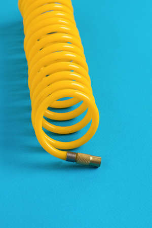 A yellow compressor hose twisted into a spiral on a blue background. minimal concept.の写真素材