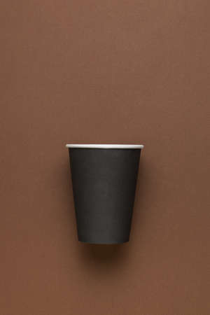 A black paper cup with a white border on a brown background. minimal concept. Drinks to take away.