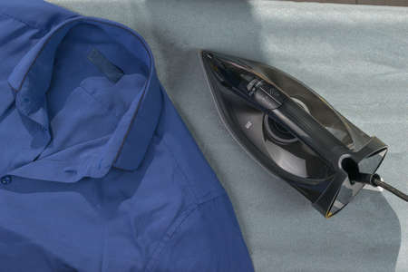 An iron and a blue men's shirt on the ironing board. Minimal concept of linen care.の写真素材