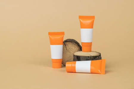 Orange tubes and an old tree on a beige background. Cosmetics and therapeutic ointments based on...