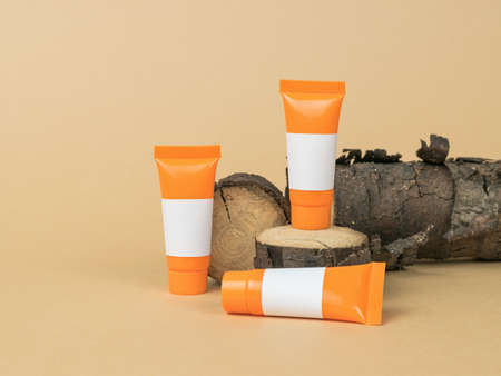 Orange tubes with white letterheads on an old tree on a beige background. Cosmetics and therapeutic...