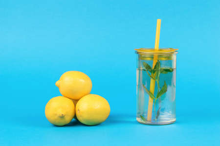 Three lemons and a glass of water with mint and lemon on a blue background. A popular refreshing...