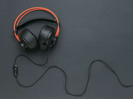 Orange and black headphones with a wire on a black background. An accessory for listening to audio recordings. flat lay.の写真素材