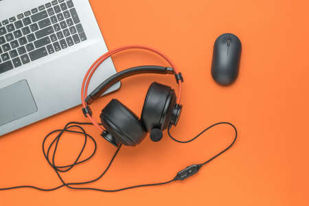 Laptop, computer mouse and black and orange headphones on an orange background. creative workplace. flat lay.の写真素材