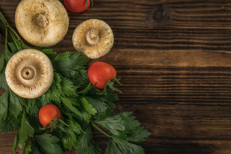 Forest mushrooms, two tomatoes and greens on a wooden background. Vegetarian food from the forest. flat lay.の写真素材