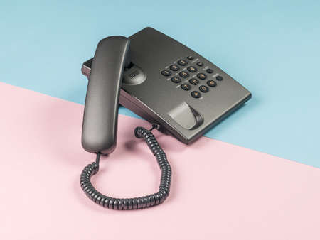 Gray push-button phone with the handset off on a pink and blue background. The concept of telephone communication.の写真素材