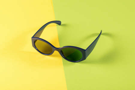 Blue sunglasses on a green and yellow background. Stylish summer accessory.