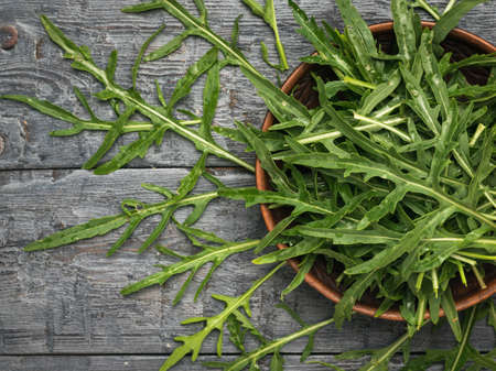 Fresh arugula grass in a bowl and on a wooden table. Vitamin vegetarian food. flat lay.