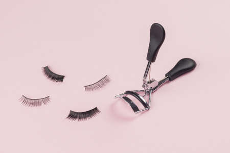 False eyelashes and curlers scattered on a pink background. Minimal makeup concept.の写真素材
