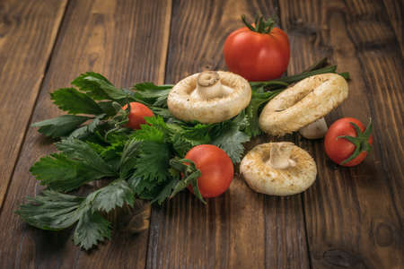 Three large mushrooms, tomatoes and parsley on a rustic table. Vegetarian food from the forest.の写真素材