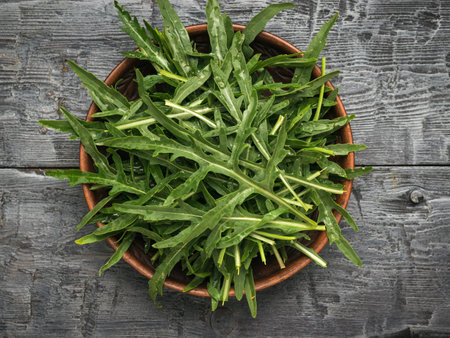 A bowl with fresh green arugula leaves on a black wooden table. Vitamin vegetarian food. flat lay.の写真素材
