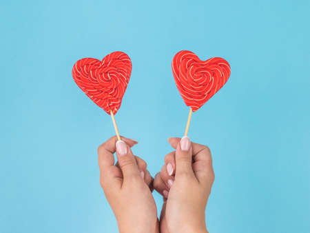 Female hands with two heart-shaped candies on a blue background. Minimal concept of sweets and love.の写真素材