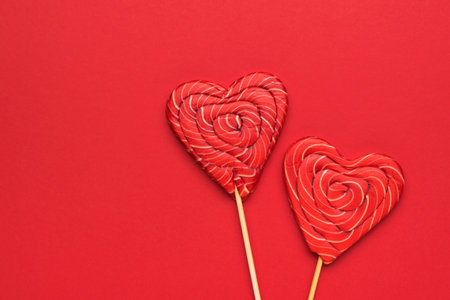Two large red heart-shaped candies on a stick on a red background. Minimal concept of sweet life and love. flat lay.の写真素材
