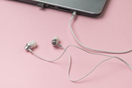 White headphones connected to a laptop on a pink background. The concept of business and education.の写真素材