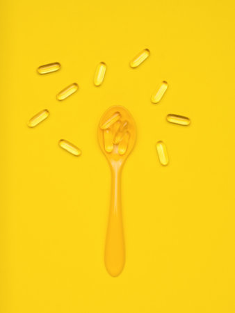 Yellow spoon and fish oil capsules on a yellow background. Biologically active additive. flat lay.の写真素材