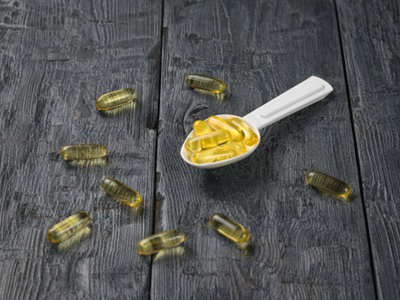 A plastic spoon with fish oil capsules on a wooden table. Biologically active additive.の写真素材