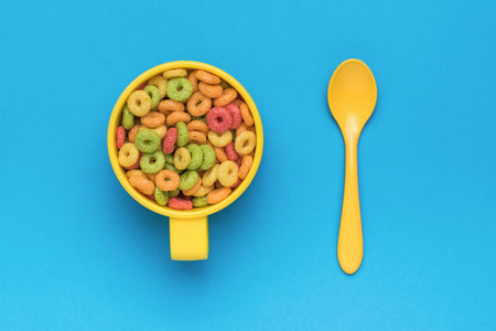 A ready-made breakfast of multicolored corn rings and a spoon on a blue background. The minimum...