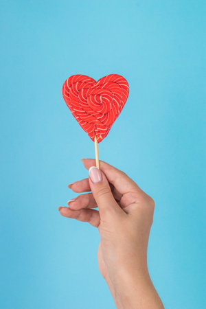 A girl's hand with a bright red candy on a blue background. Minimal concept of sweets and love.の写真素材