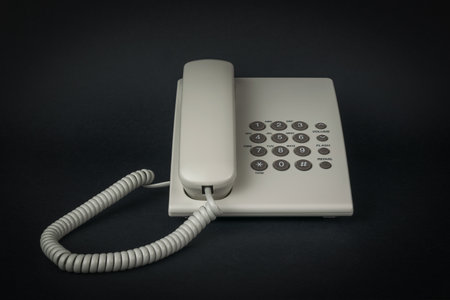 A white landline phone with buttons on a black background. The concept of telephone communication....