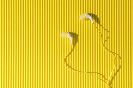 Yellow and white headphones for a smartphone on an abstract yellow background. Minimal concept of mobile devices.の写真素材