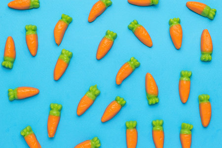 Scattered on a blue background are small sweets in the form of carrots. Minimal harvest concept. creative photo. flat lay.の写真素材
