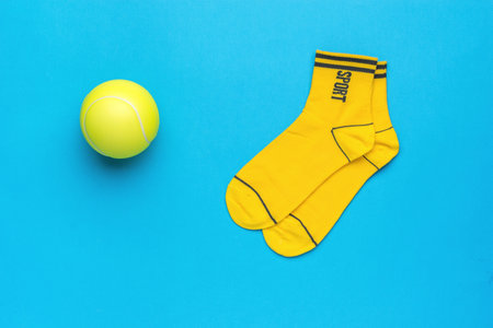 Yellow ball and bright yellow socks on a light blue background. A stylish sports accessory. flat...
