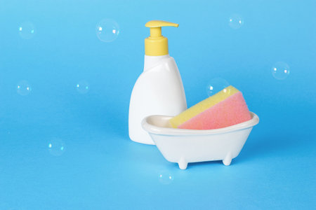 Foam sponge on a stand and detergent on a blue background. Minimal concept of washing and cleaning.