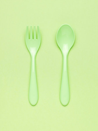 Green plastic spoon and fork on a light green background. Minimal concept of plastic tableware. flat lay.の写真素材