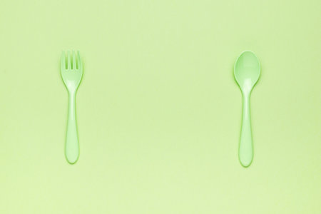 A green set of plastic forks and spoons on a green background. A place for your text. Minimal concept of plastic tableware. flat lay.の写真素材