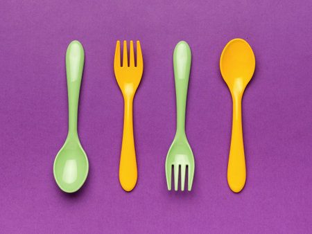 Green and yellow plastic spoons on a purple background. Minimal concept of plastic tableware. flat lay.の写真素材