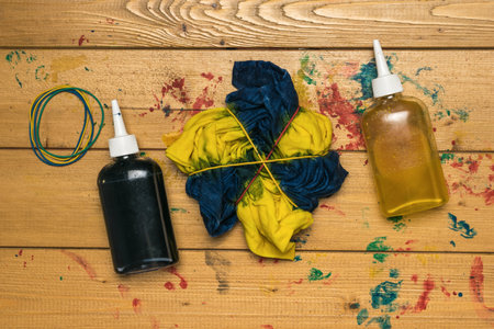 Twisted white T-shirt painted in blue and yellow in tie dye style. The process of painting in the style of tie dye. flat lay.の写真素材
