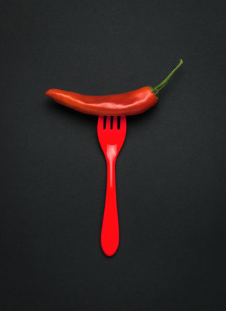 Hot red pepper on a red plastic fork on a black background. A popular spice. flat lay.の写真素材
