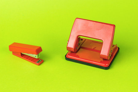 A red hole punch and a red stapler on a green background. Minimal stationery concept.の写真素材