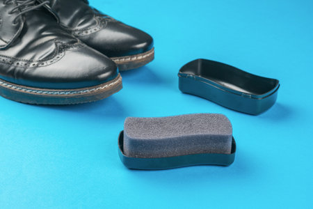 Black men's shoes and foam sponge on a blue background. Minimal shoe care concept.の写真素材