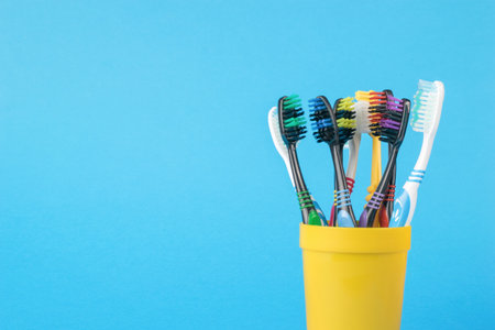 A set of toothbrushes in a yellow plastic cup on a blue background. Minimal oral care concept.の写真素材