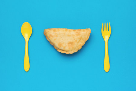 Yellow spoon and fork and meat pie on a blue background. The minimum concept of bakery products with meat.の写真素材