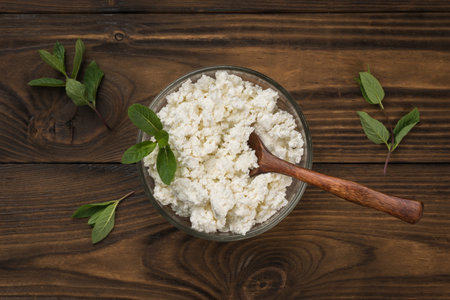 Top view of a bowl with cottage cheese and a wooden spoon on a wooden table. Minimal concept of natural dairy products.の写真素材