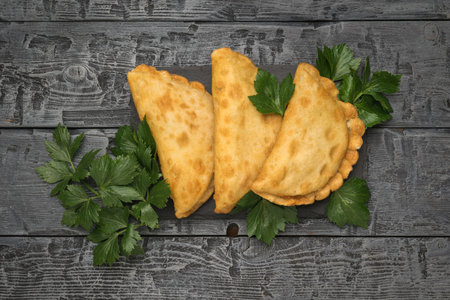 Three chebureks and spicy herbs on a wooden background. The minimum concept of bakery products with...