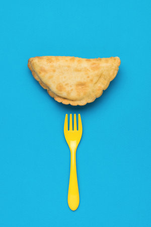 Yellow fork and fresh cheburek on a blue background. The minimum concept of bakery products with meat.の写真素材