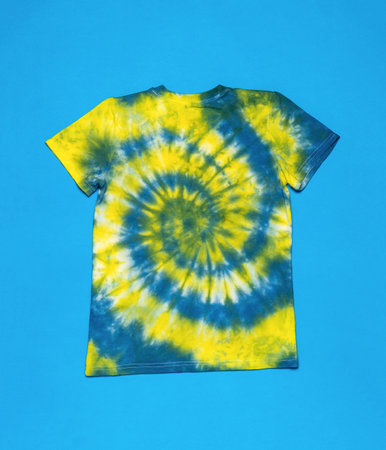 T-shirt with a yellow-blue spiral pattern on a blue background. The background on the fabric is made with your own hands. flat lay.の写真素材
