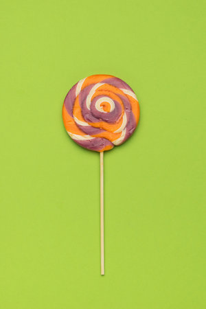 A large, round, colored lollipop on a green background. Minimal concept of sweet life and love. flat lay.の写真素材