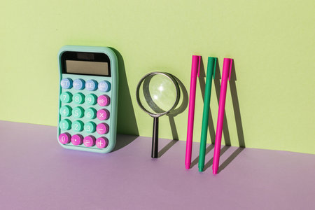 Calculator, magnifying glass and a set of pens on a purple-green background. The concept of financial accounting. Flat lay.の写真素材