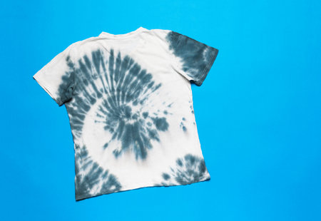 T-shirt decorated in tie dye style on a bright blue background. The concept of self-dyeing clothes. Flat lay.の写真素材