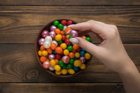 The girl takes a candy from a cup on a wooden table. Sweet treat.の写真素材