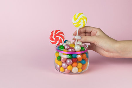 The girl's hand takes a lollipop on a stick from a glass jar. Sweet treat.の写真素材