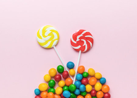 Two lollipops and a bunch of colorful candies on a pink background. The concept of sweets. Flat lay.の写真素材