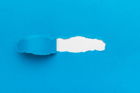 A torn blue paper from under which a white one peeks out. The concept of finding new opportunities.の写真素材