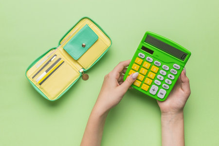 The hands of a girl with a calculator and a wallet on a green background. The concept of budget management. Flat lay.の写真素材