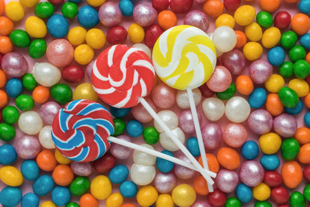 Three round lollipops on a stick on a background of colorful candies. The concept of sweets. Flat lay.の写真素材